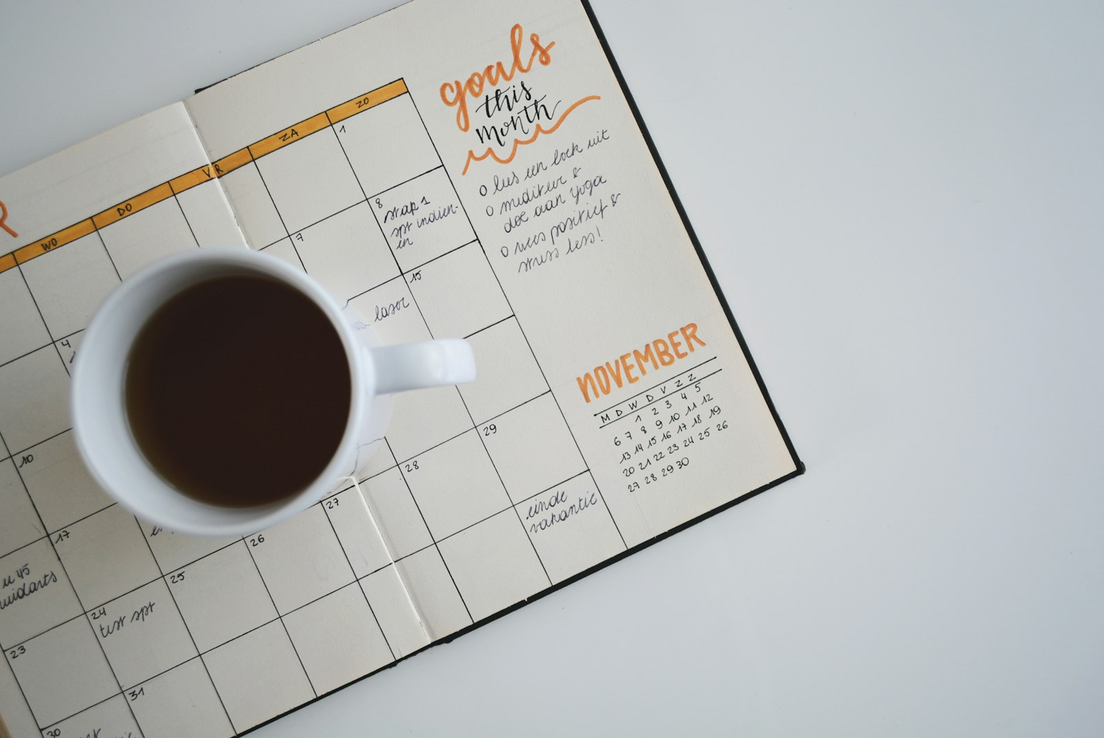 Hand notiert Termine in einem Planer neben einer Tasse Kaffee